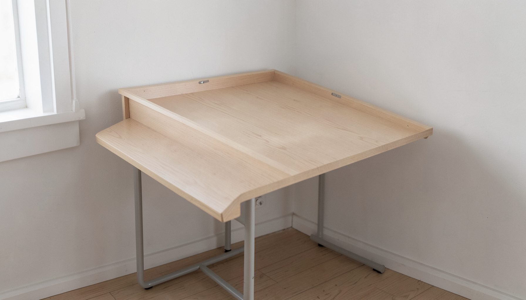 A compact fold-out table against a wall in a small apartment, clean minimalist design with light wood surface