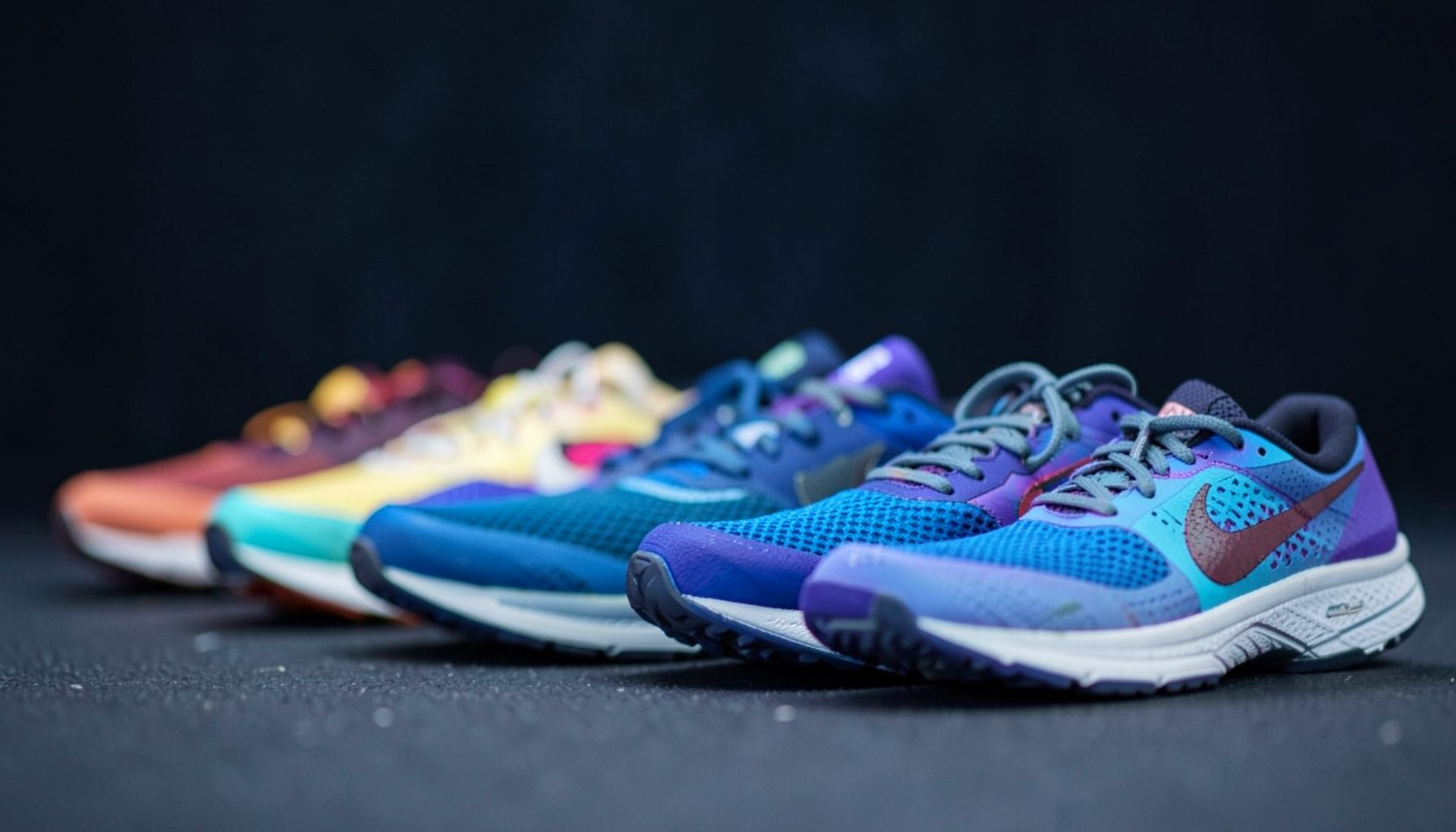 A row of colorful Nike running shoes in soft focus against a dark athletic backdrop, with deep navy and muted gray tones