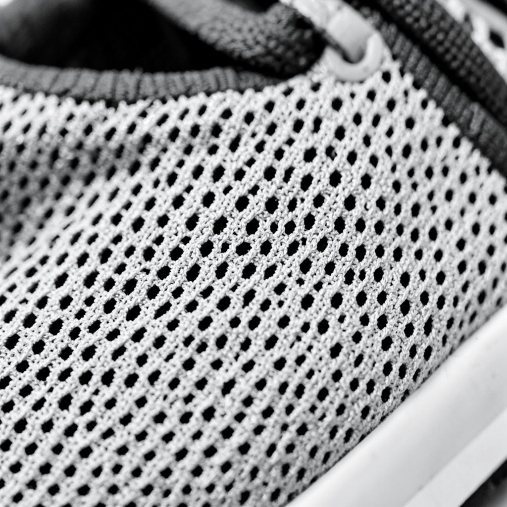 Monochrome close-up of a running shoe's breathable mesh upper, emphasizing texture and weave pattern in black and white